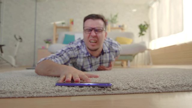 young man had a heart attack and he tries to reach the smartphone lying on the floor