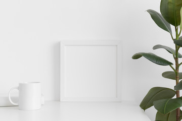 White square frame mockup with a mug, book and ficus on a white table.