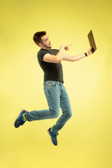 Weightless. Full length portrait of happy jumping man with gadgets isolated on yellow background. Modern tech, freedom of choices concept, emotions concept. Using tablet for selfie or vlog in flight.