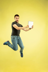 Weightless. Full length portrait of happy jumping man with gadgets isolated on yellow background. Modern tech, freedom of choices concept, emotions concept. Using tablet for selfie or vlog in flight.