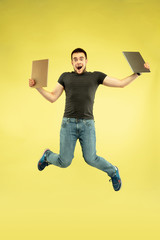 Weightless. Full length portrait of happy jumping man with gadgets isolated on yellow background. Modern tech, freedom of choices concept, emotions concept. Using tablet for selfie or vlog in flight.