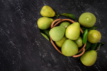 Fresh pomelo,grapefruit in bamboo basket with green leaf on dark black slate background. Seasonal fruit for Mid-Autumn Festival. Top view. Flat lay.