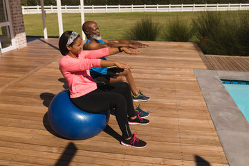 Senior couple performing balancing on exercise ball in the backyard