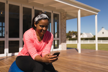 Fototapeta premium Woman using mobile phone while sitting on exercise ball in the backyard