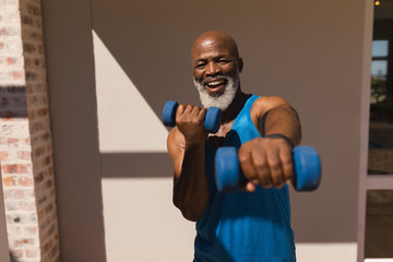 Senior man training arms with dumbbells in the backyard of home