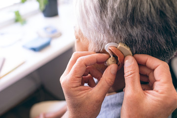 Male doctor applying hearing aid to senior woman  - obrazy, fototapety, plakaty