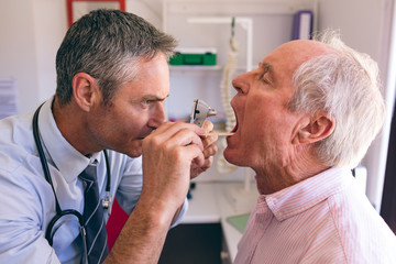 Male doctor checking senior male patient mouth with otoscope