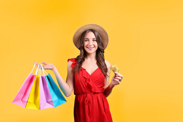 Black friday season sale concept. Attractive young woman with long brunette hair, wearing straw hat, holding many different blank shopping bags over yellow isolated background. Copy space, close up