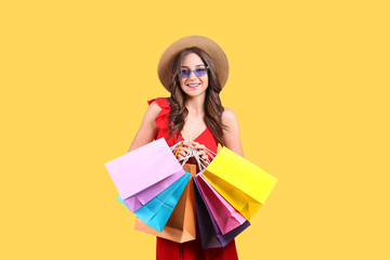 Black friday season sale concept. Attractive young woman with long brunette hair, wearing straw hat, holding many different blank shopping bags over yellow isolated background. Copy space, close up
