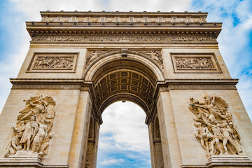 Fototapeta na wymiar Great low angle shot of the stately Arc de Triomphe seen from the east with the two sculptures Le Départ and Le Triomphe with a dramatic blue sky. It is one of the most famous monuments in Paris.