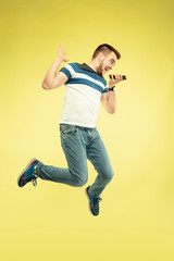 Fototapeta na wymiar Full length portrait of happy jumping man with gadgets on yellow background. Modern tech, freedom of choices concept, emotions concept. Using smartphone for voice messege or videocall in flight.