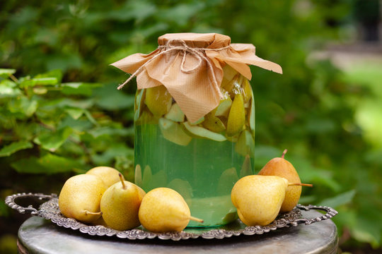 Pears compote in a big glass jar. Traditional russian recipe. Rustic decor, metal vintage tray. Fresh ripe pears from the garden near the jar. Green background. Russia, Moscow