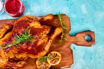 Baked whole chicken with sauces on wooden board on blue background. Christmas chicken. Dinner. Appetizer..