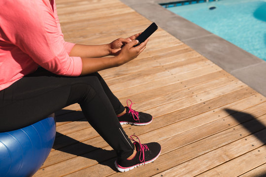 Woman using mobile phone while sitting on exercise ball in the backyard of home