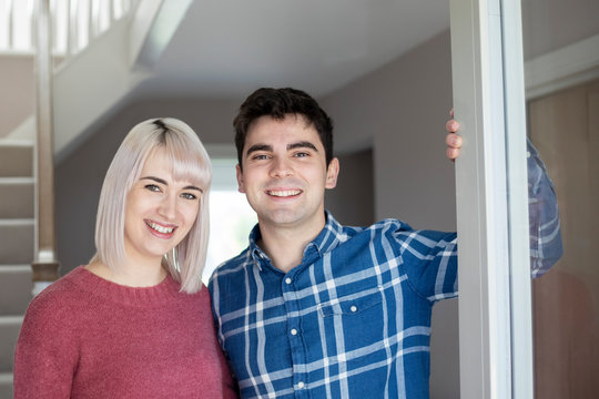 Portrait Of Smiling Young Couple Opening Front Door Of New Home