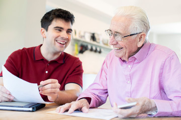Young Man Helping Senior Neighbor With Paperwork At Home