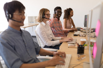 Executives working on personal computer while talking on headset in office