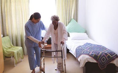 Female nurse helping senior female patient to stand with walker