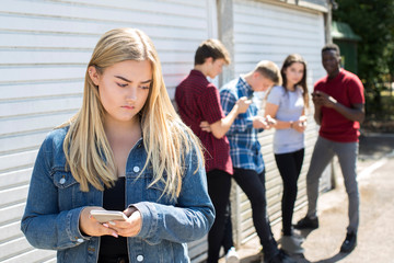 Unhappy Teenage Girl Being Bullied By Text Message Outdoors