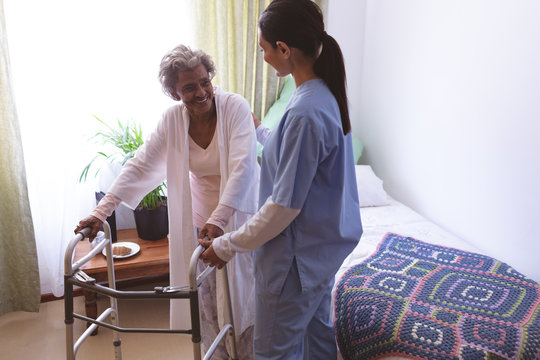 Female Nurse Helping Senior Female Patient To Stand With Walker