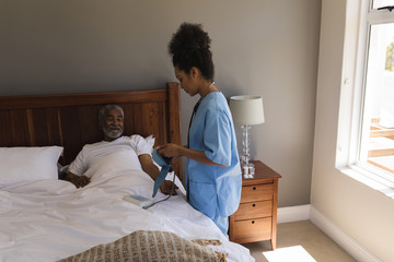 Female doctor measuring blood pressure of senior man in bedroom