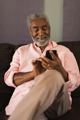 Senior man using mobile phone in living room at home