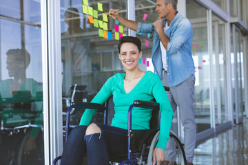 Disabled businesswoman looking at camera while male executive writing on sticky notes