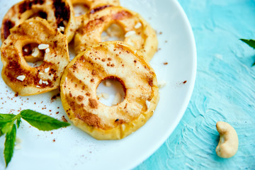 Grilled apples with cinamon on white plate on blue background. Grilled dessert. Barbecue fruit. Copy space. Healthy food. Vegan food.
