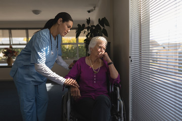 Female doctor consoling sad disable senior woman at nursing home
