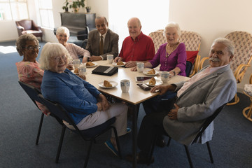Front view of happy group of senior friends sitting on dining table and looking at camera