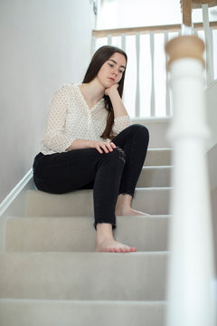 Fed Up Teenage Girl Sitting On Stairs At Home