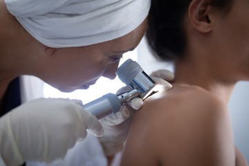 Female doctor checking woman body with dermatoscopy