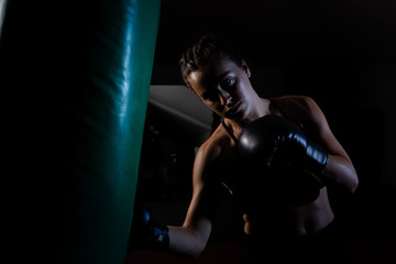 Fototapeta na wymiar Young female boxer punching a bag on a sports training in a gym.
