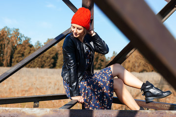 Portrait of a  cheerful woman in a knitted hat,  leather coat, pretty dress and boots, smiles cute,...