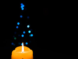 Glowing Christmas candle with blue Christmas lights in shape of Christmas tree in the background.