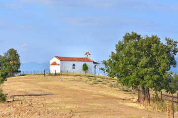 Picturesque autumn landscape with a wooden white house with a red roof on a hill with yellow grass surrounded by trees on blue sky background. Farm on a mountain. 