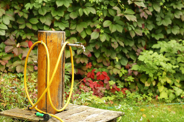 water well creative outlet with hose close up photo on green summer garden background