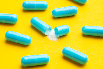 Blue tablets in capsules. One capsule is open. Yellow background.
