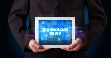 Young business person working on tablet and shows the inscription: TECHNOLOGY NEWS