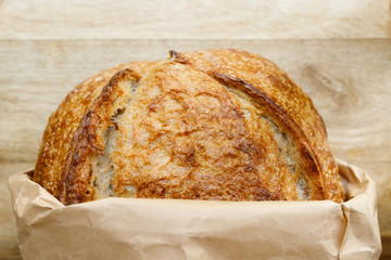 fresh sourdough baked bread in a craft bag on a wooden table. Close up. Horizontal frame. Home bakery concept.