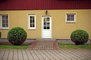 Yellow house front door with red roof and neat bushes