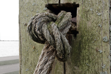 Old textured rope knot on aged wooden post background