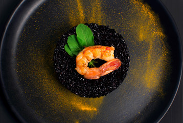 Black rice risotto with Shrimp and safron in a black plate seen from above in dark background close