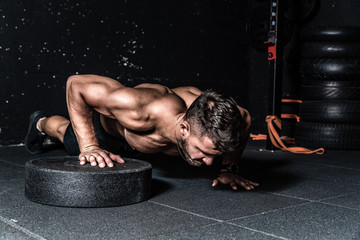 Young strong sweaty focused fit muscular man with big muscles doing push ups with one hand on the barbell weight plate for training hard core workout in the gym real people selective focus - Powered by Adobe