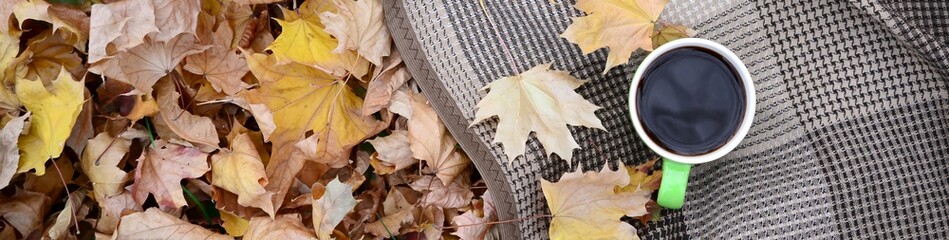 Naklejka na ściany i meble Autumn leaves and hot steaming cup of coffee lies on checkered plaid outdoors