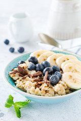 Oat porridge with banana, chocolate and fresh blueberry in a bowl on a light gray slate, stone or concrete background. Top view.