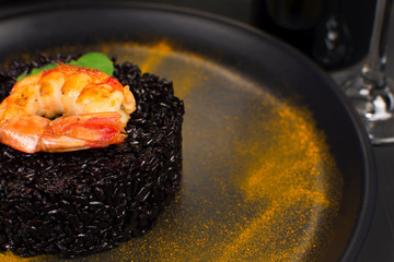 Black rice risotto with shrimp and safron in a black plate in dark background close