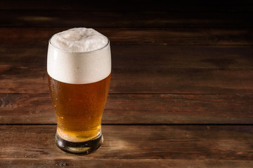 Glass of light beer on a dark pub. Glass beer on wood background with copy space. Full glass with lager beer, close up