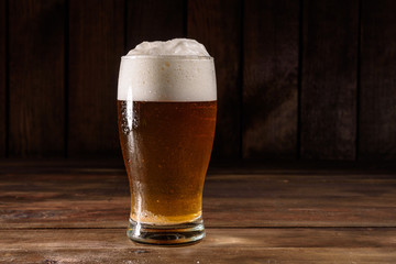 Glass of light beer on a dark pub. Glass beer on wood background with copy space. Full glass with lager beer, close up