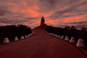 Russia, Murmansk, Barents Sea: Famous Alyosha Monument to Soviet soldiers, sailors and airmen of World War II (the Great Patriotic War 1941-1945) from behind against sun with dramatic blood red sky.